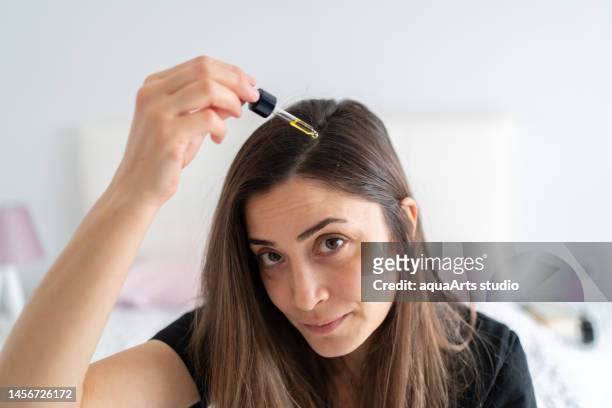 portrait of applying hair serum to her hair - human hair stock pictures, royalty-free photos & images