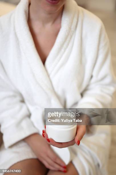 cosmetic skin care products in a hands of a women wearing white bathrobe. - robe tube stock pictures, royalty-free photos & images