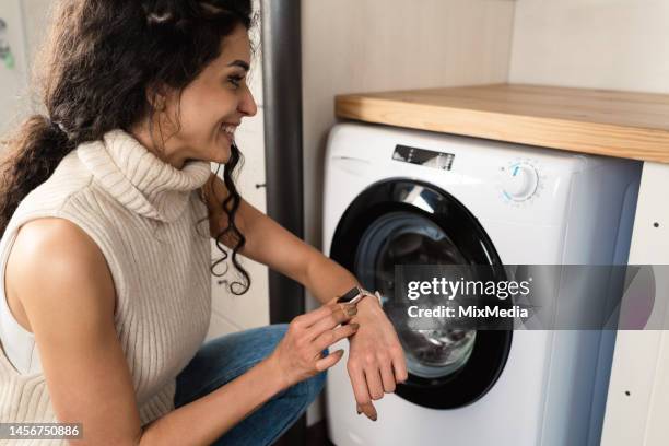 young woman turning on her washing machine using a smart watch - clothes on clothes off photos 個照片及圖片檔
