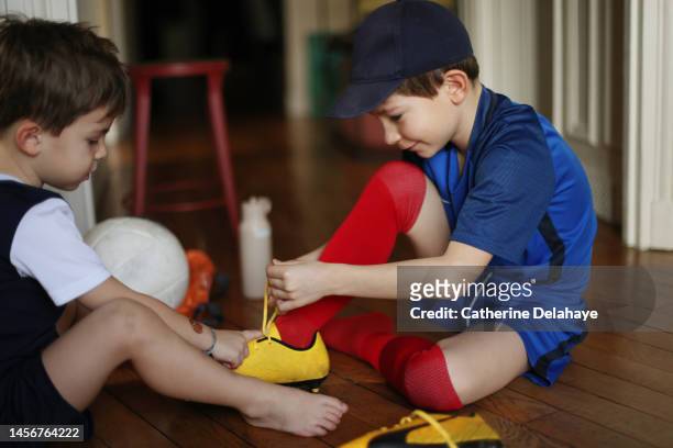 a 7 year old boy, dressed as a footballer, preparing for sports. his little brother helping him. - boy tying shoes stock-fotos und bilder