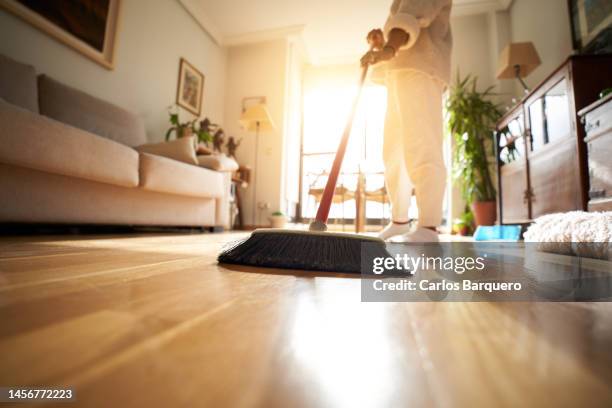 unrecognizable woman sweeping the parquet floor, window light reflection. - clean bildbanksfoton och bilder