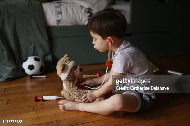 a 4 year old boy playing doctor with his teddy bear in his bedroom - kids imagination photos et images de collection