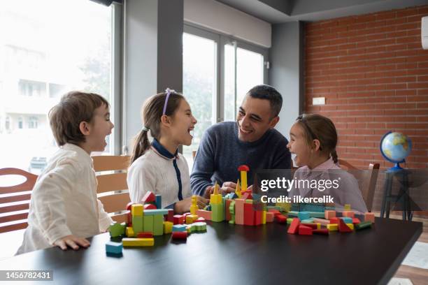 father and children playing with toy blocks at home - playroom stock pictures, royalty-free photos & images