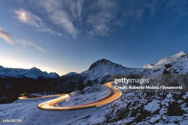 lights of car trails on snowy mountain road at dusk - berninapass stock pictures, royalty-free photos & images