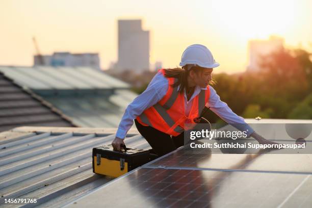 asian female technician checking the maintenance of the solar panels on rooftop of the building, engineering team working on checking and maintenance in solar power plant to innovation of green energy for life on factory roof. - solar panel city stock-fotos und bilder