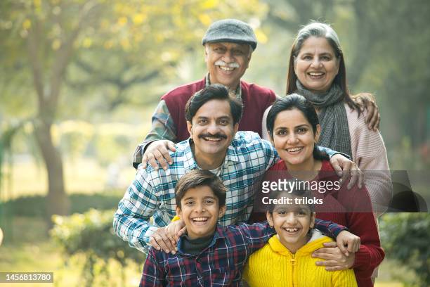 fröhliche mehrgenerationenfamilie, die rücken an rücken im park steht - indian family stock-fotos und bilder