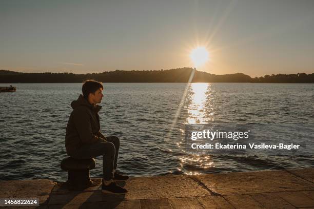 a man sits on the embankment and looks at the sunset - one embankment stock-fotos und bilder