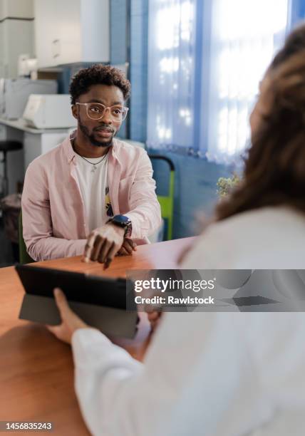 vertical photo of a man in a doctor's office pointing to a digital tablet and looking at the doctor attentively - digital techniques ストックフォトと画像