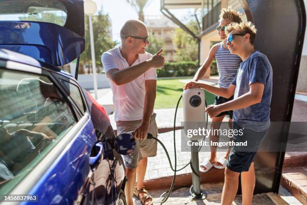 father and teenage sons charging the electric car. - plugging in stock pictures, royalty-free photos & images