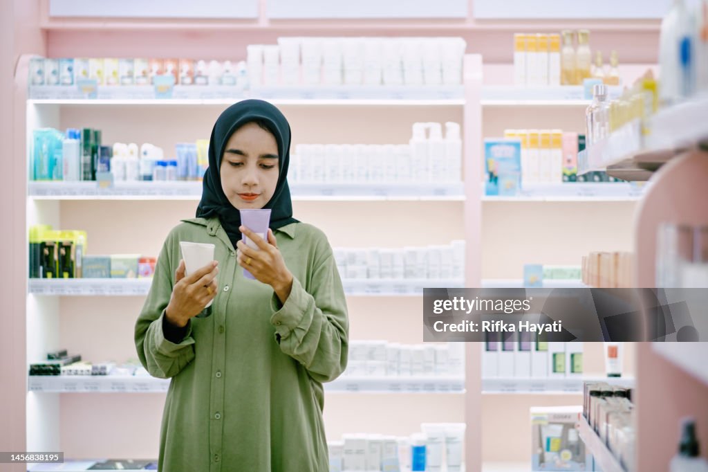 Asian hijab woman standing in beuty care store while holding some product on her hands.