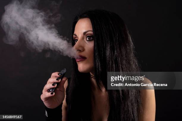 young woman in her thirties poses in studio and fashion photos on black background with fashionable accessories, smoking with vaporizer electronic cigar head shot - intim piercing bildbanksfoton och bilder