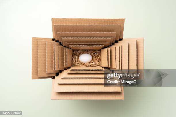 an egg packed in multiple nested cardboard boxes, excessive packaging - fragilità foto e immagini stock