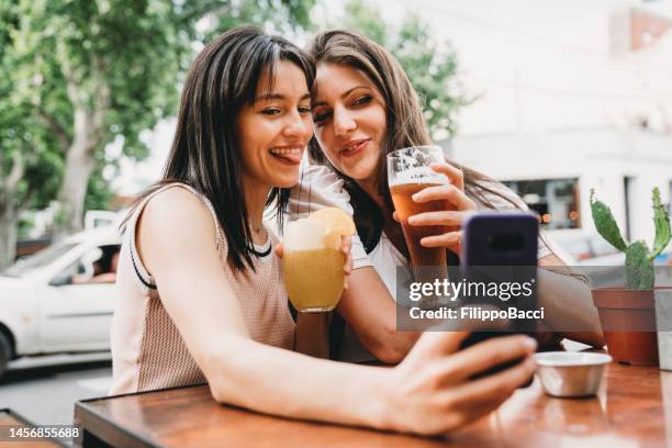zwei freundinnen sitzen in einem café, trinken bier und cocktails und machen gemeinsam ein selfie - palermo buenos aires stock-fotos und bilder