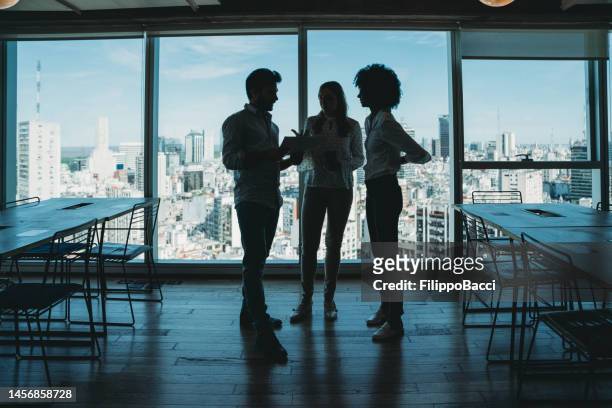 silhouette von drei geschäftsleuten in einem modernen büro. skyline der stadt im hintergrund - buenos aires people stock-fotos und bilder
