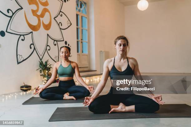 young women meditating in a yoga studio - lotus position imagens e fotografias de stock