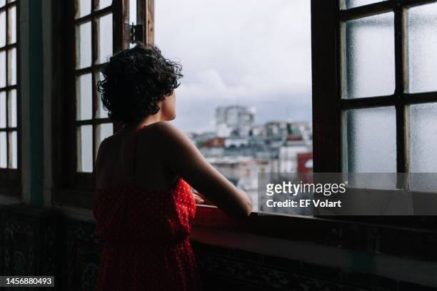 pensive young latin girl contemplating the city through window at home - greater antilles stock pictures, royalty-free photos & images