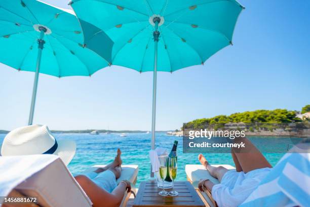 two women relaxing at the beach with champagne. - deckchair stock pictures, royalty-free photos & images