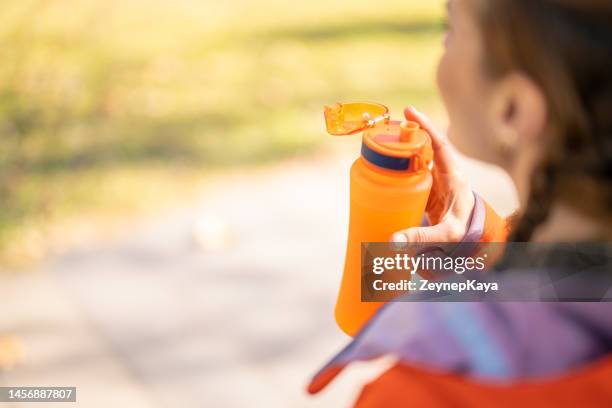 young woman drinking orange color sports drink, outdoor exercises - energy drink stock pictures, royalty-free photos & images