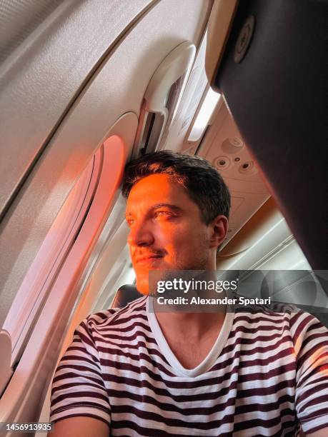 young man looking out of the airplane window during flight at sunset - genomen met mobiel apparaat stockfoto's en -beelden