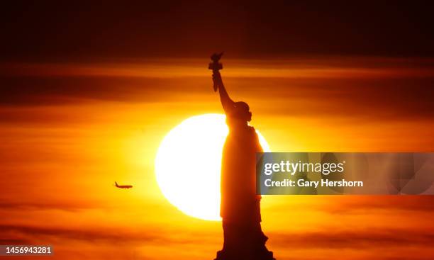 The sun sets behind the Statue of Liberty as an airplane flies past on January 16 in New York City.