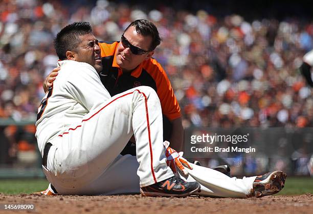 Hector Sanchez of the San Francisco Giants grimaces in pain on the ground after fouling a ball off his shin as head athletic trainer Dave Groeschner...