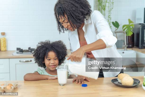 african american daughter and mother drink milk at kitchen home - moeder kind zes melk stockfoto's en -beelden