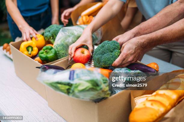 unrecognizable food bank volunteers unpack donation box - food distribution stock pictures, royalty-free photos & images