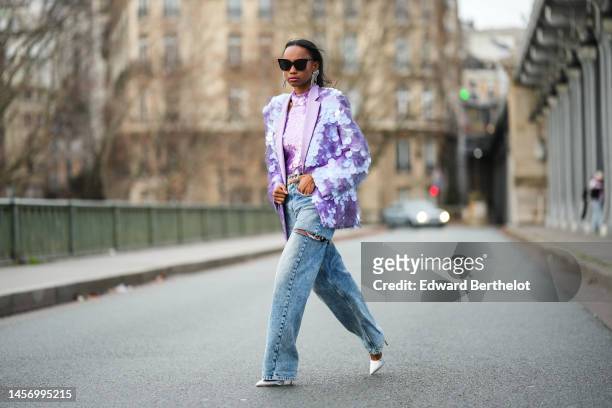 Emilie Joseph @in_fashionwetrust wears black sunglasses, fringed rhinestones long earrings, a purple large sequins halter neck / tank-top, a matching...
