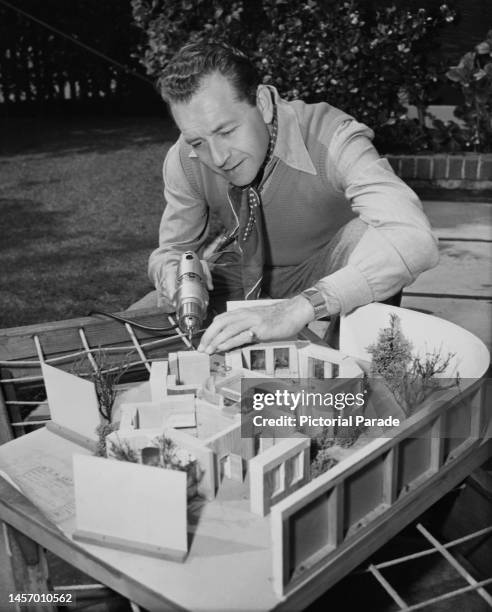 Austrian actor, film producer, screenwriter and film director Paul Henreid , wearing a neckerchief and tanktop, using a power drill to construct an...