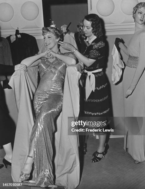 American singer and actress Jeanette MacDonald relaxes in her 'up-right chair' which protects her rhumba gown of blue sequins, as hairdresser Olga...