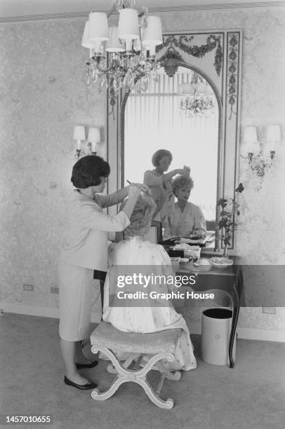 American actress and comedian Lucille Ball having her hair styled by an hairdresser, reflected in the mirror on a dressing table in Ball's apartment...
