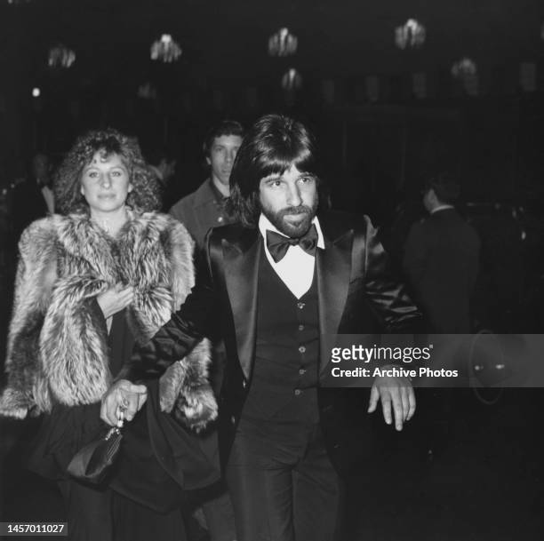 American singer and actress Barbra Streisand, wearing a fur coat. And holding the hand of her partner, American film producer John Peters, after...
