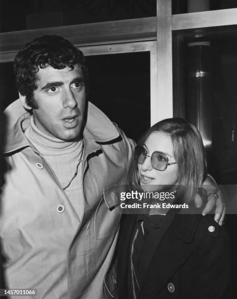 American actor Elliott Gould, wearing a raincoat, and his wife, American singer and actress Barbra Streisand, wearing large sunglasses, attend a...