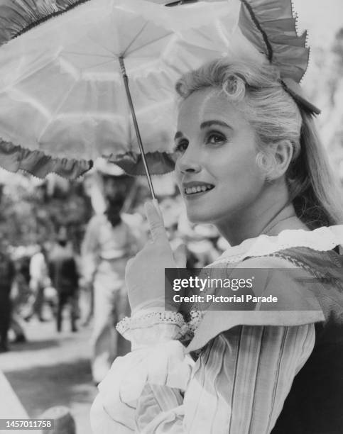 American actress Eva Marie Saint, in costume as she shades herself beneath a parasol during a break in filming of the historical romance 'Raintree...