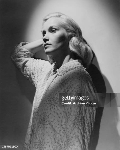 American actress Eva Marie Saint, her right hand behind her head as she stands, wearing night clothes, against a wall across which shadows are cast...