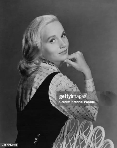 American actress Eva Marie Saint wearing a black dress over a pattered shirt, her chin resting on her right hand, in a studio portrait against a grey...