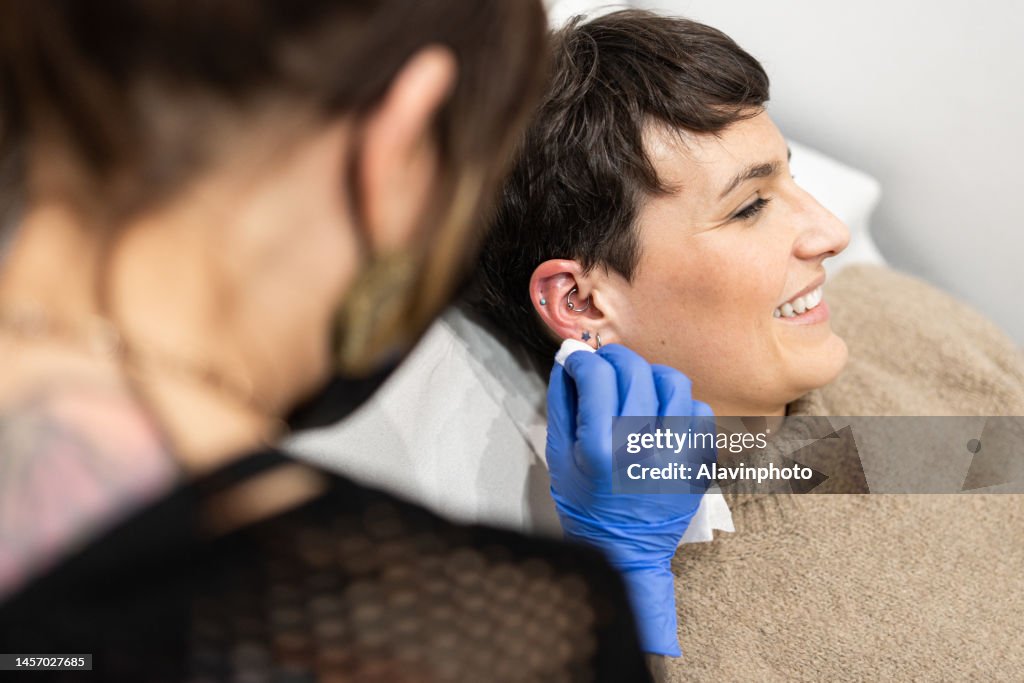 Piercer cleaning client's ear in preparation for piercing