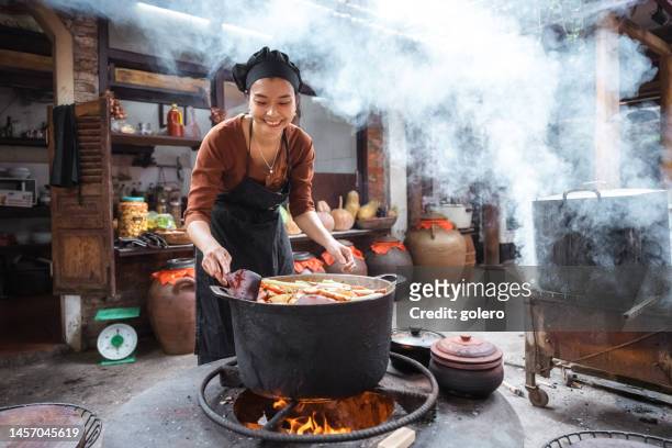 レストランで暖炉で料理をする若い笑顔のベトナム人女性シェフ - vietnamese culture ストックフォトと画像