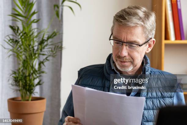 white 50 year old businessman working with paperwork at home office - argumentista imagens e fotografias de stock