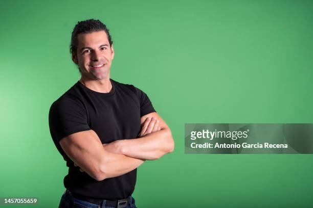 portrait of man on green background with arms crossed looking at camera, smiling happy with basic black shirt - chroma key fotografías e imágenes de stock
