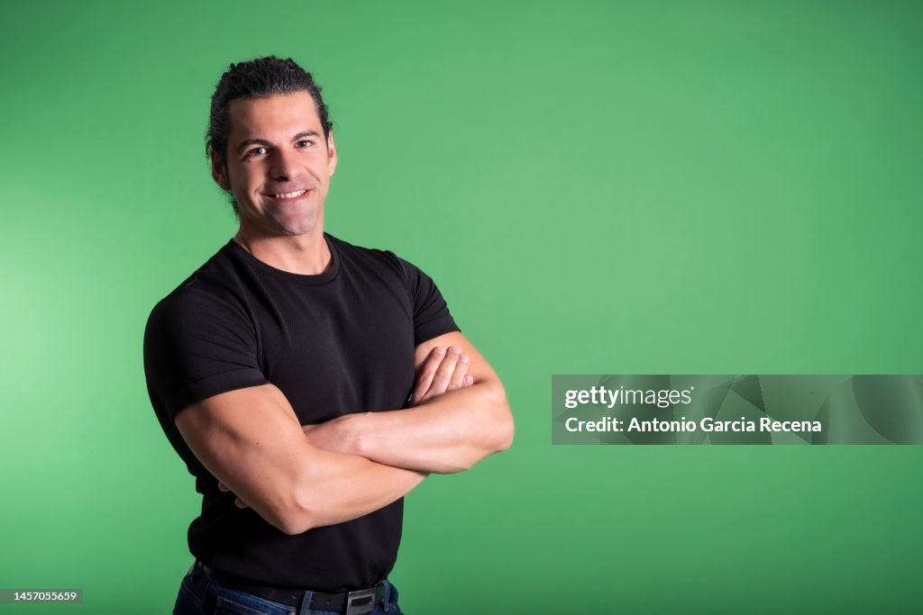 Portrait of man on green background with arms crossed looking at camera, smiling happy with basic black shirt