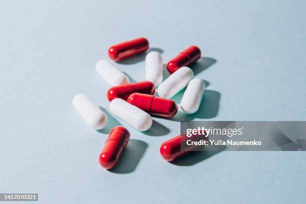 red and white capsule pills on blue background with hard light and shadows. - generic drug stock pictures, royalty-free photos & images