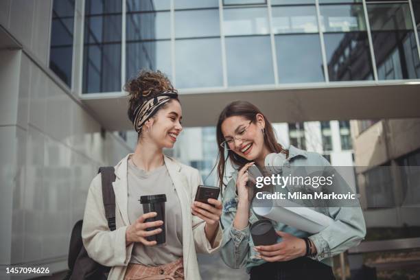 zwei befreundete studentinnen laufen vor dem fakultätsgebäude, sie sind in einer pause zwischen den vorlesungen - unileben stock-fotos und bilder