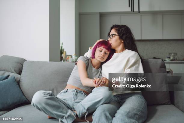 wise advice from mother. woman embracing her teenage girl on a couch - girls holding hands stock pictures, royalty-free photos & images