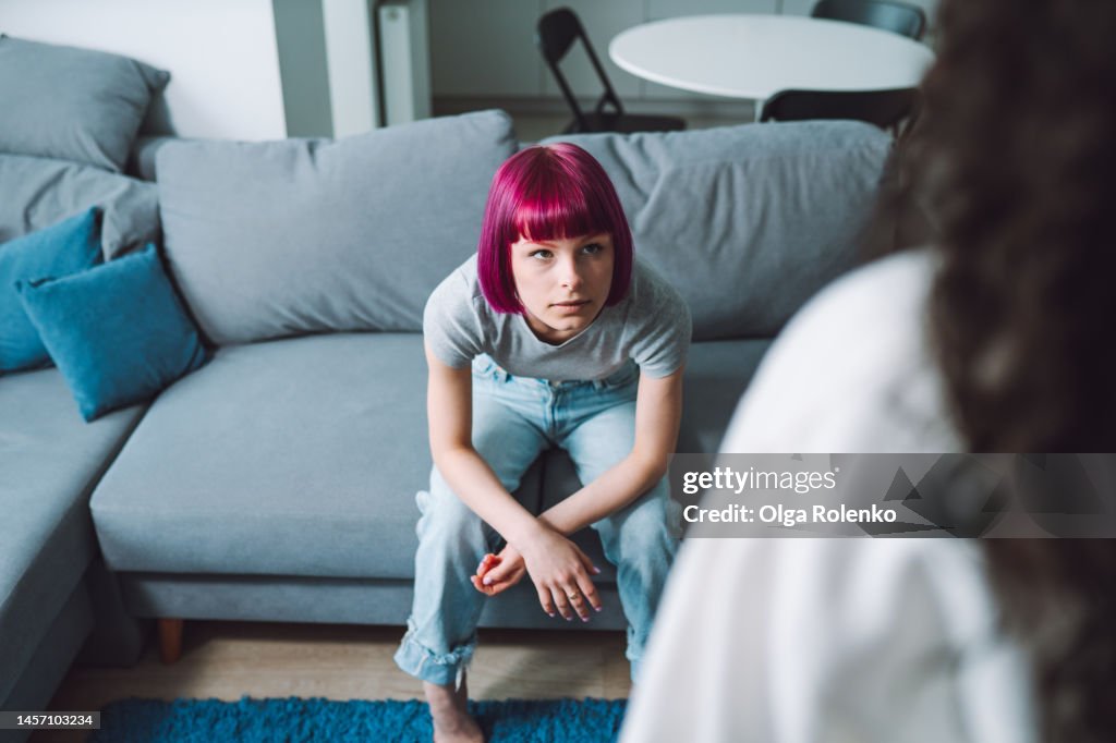 Trust problem in family. Teen girl looking at an unrecognizable woman with anger, sitting on a couch