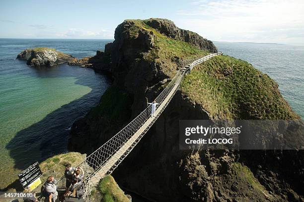 In this handout image provided by LOCOG, Torchbearer Denis Broderick holds the Olympic Flame on the Carrick-a-Rede rope bridge which links the...