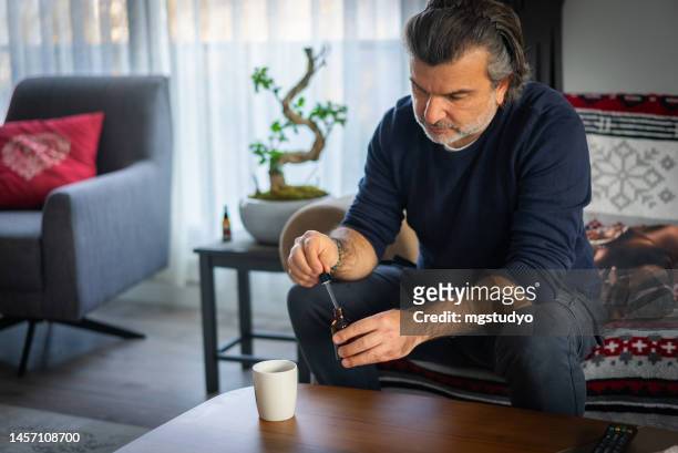 sick man adding cbd oil to morning tea at home - cbd oil stock pictures, royalty-free photos & images