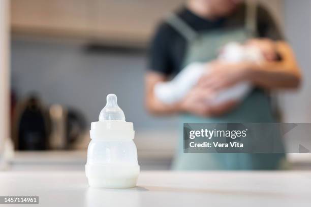 close-up view of unrecognizable single dad with baby at kitchen counter feeding milk bottle to newborn. - formula ストックフォトと画像