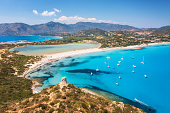 Aerial view of beautiful sandy beach, old tower on the hill, sea bays, mountains at summer sunny day. Porto Giunco in Sardinia, Italy. Top view of blue sea with clear water, white sand, mountains