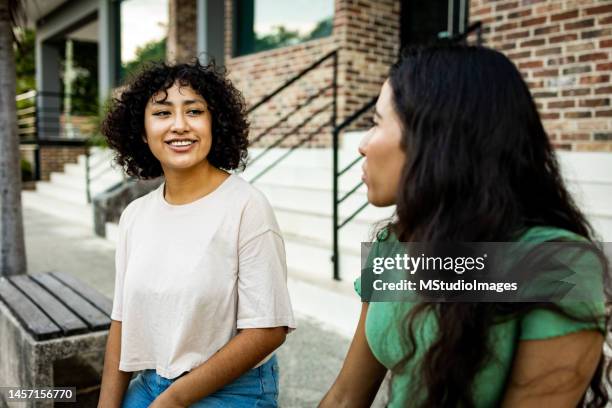 dos mujeres sentadas en el banco y hablando - amigos charlando fotografías e imágenes de stock